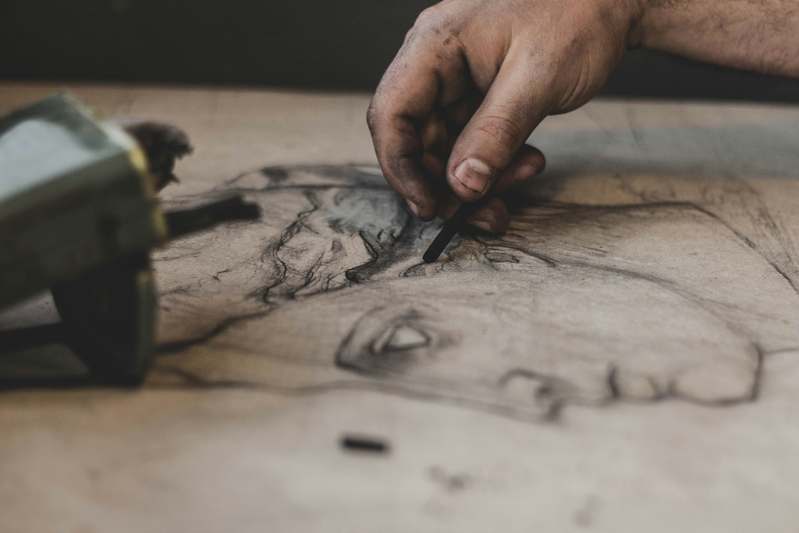 Close-up of hands holding a sketchbook and graphite pencils on a wooden desk